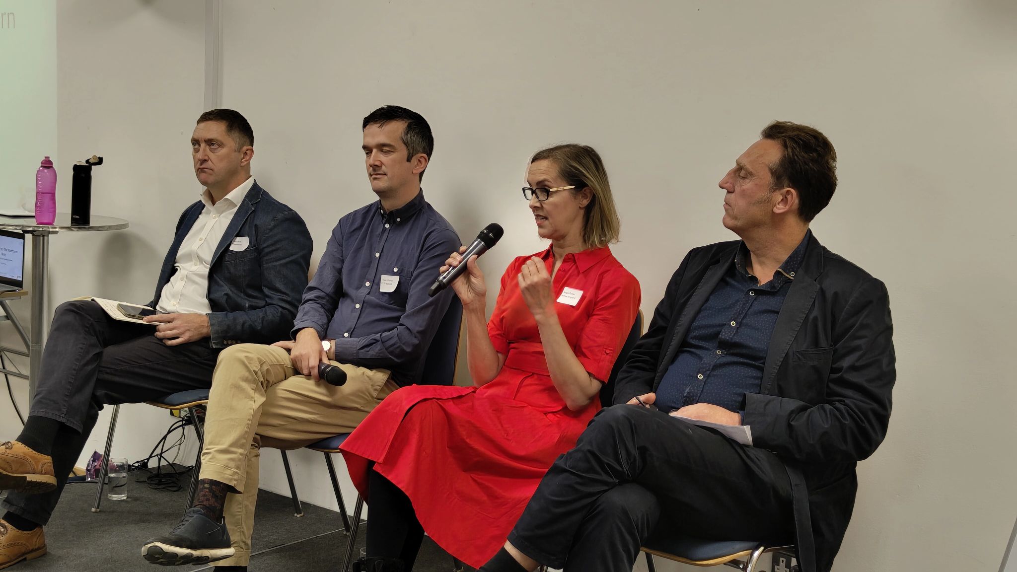 Four panellists, including Tom Chance are seated in a row speaking on a panel at the Northern Way Summit. one of them is speaking into a microphone and the other three people in the image are listening. 
